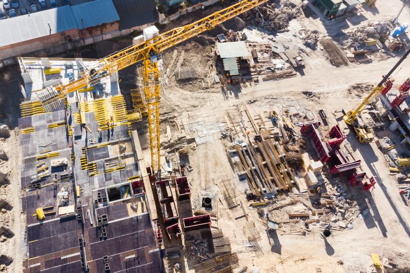 Luftaufnahme einer Straßenbau-Baustelle mit Kränen, Materialien und teilweise errichteten Strukturen auf sandigem Boden.