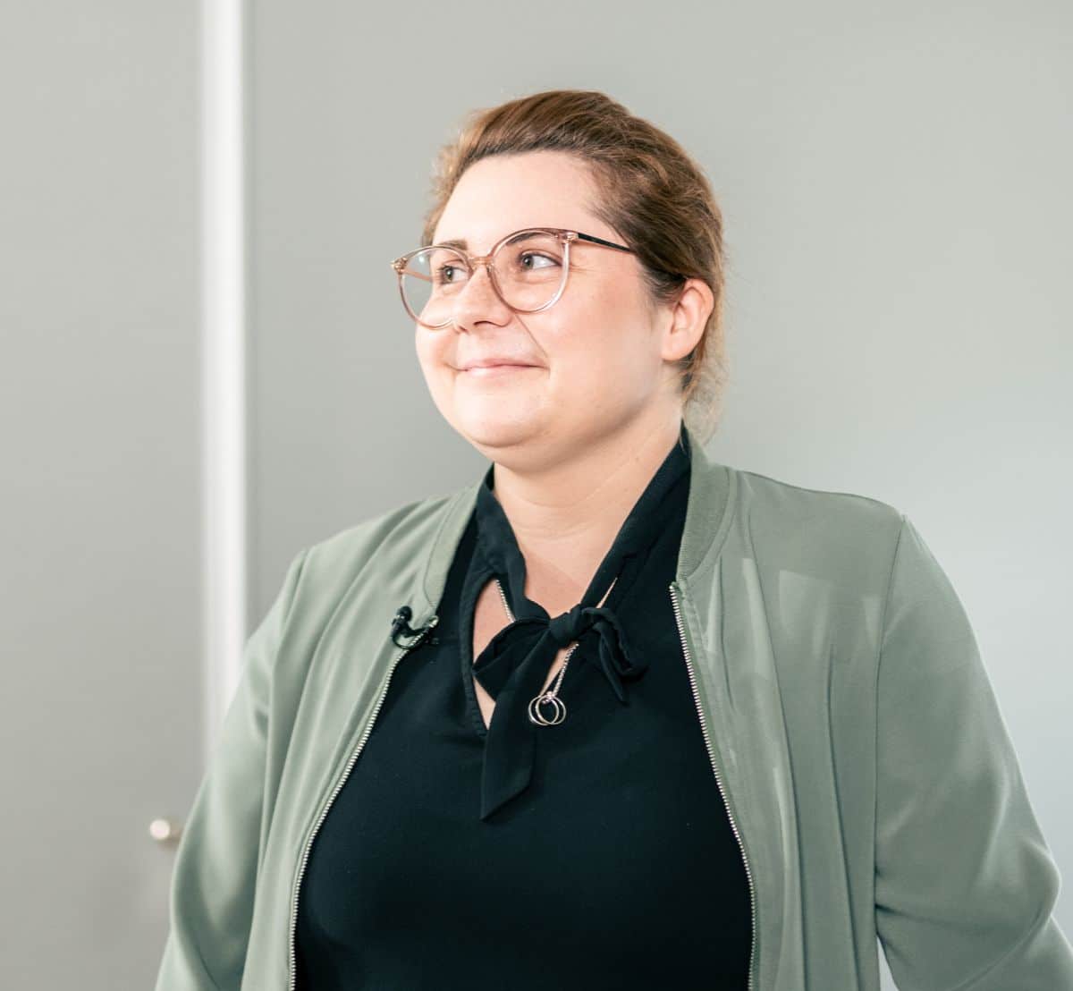 Eine Frau mit Brille und grüner Jacke blickt lächelnd nach oben und denkt kurz an die innovativen Recyclingbemühungen bei Straßenbau.