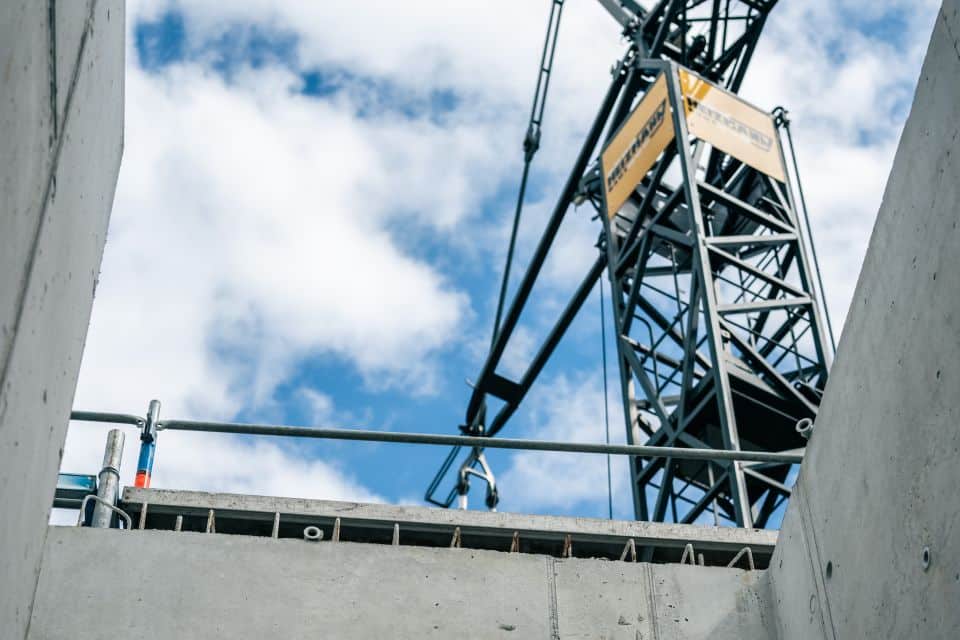 Blick auf einen Baukran und eine Gebäudestruktur vor einem teilweise bewölkten Himmel, der die Expertise eines führenden Bauunternehmens sowohl bei Tiefbau- als auch bei Straßenbauprojekten zeigt.