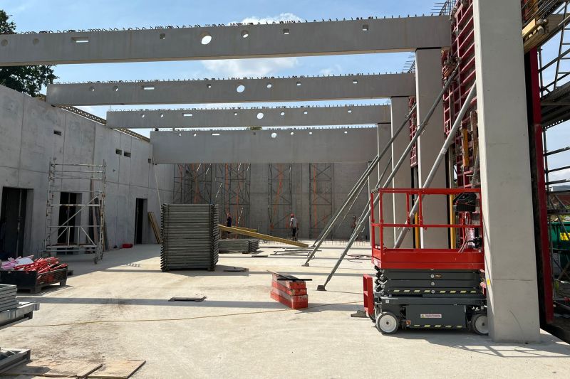 Baustelle mit Betonwänden, Stahlträgern, Gerüsten und Baumaschinen unter einem klaren, blauen Himmel. Dieses fortschrittliche Bauunternehmen legt in jeder Phase seiner Projekte Wert auf Recycling.